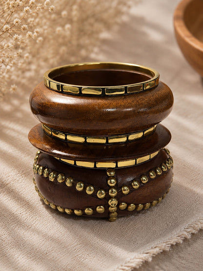 Close-up top view of stacked wooden bangles showing gold rectangular tile trim and cross-pattern gold stud embellishment