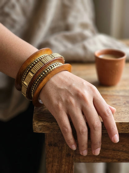 Close-up of wood and brass bangle set stacked on a woman's wrist resting on a wooden table beside a clay chai cup