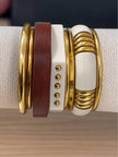 Close-up of gold-toned bangle stack with wood, white resin stud cuff, and coil resin piece on a display roll