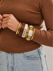 Gold-toned bangle stack worn on a wrist paired with a brown ribbed long-sleeve top and jeans