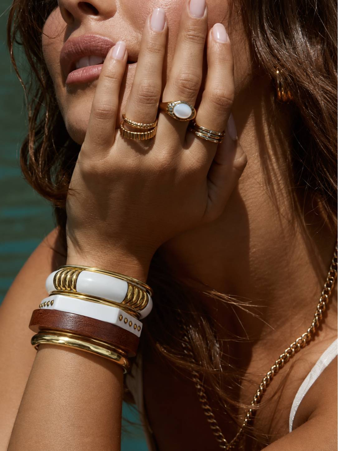 Close-up of gold-toned bangle stack on model's wrist alongside stacked gold rings and a gold chain necklace