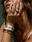 Close-up of gold-toned bangle stack on model's wrist alongside stacked gold rings and a gold chain necklace