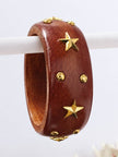 Reddish-brown lacquered wooden bangle with gold-tone star charms and round studs hung on a white display rod
