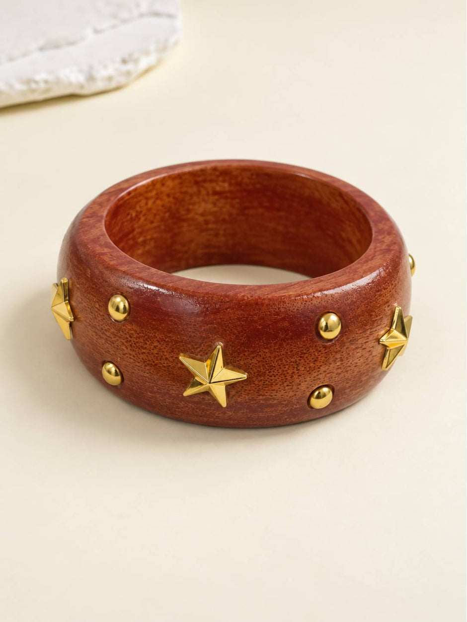Top-down view of gold-tone star-studded wooden bangle laid flat on a cream background