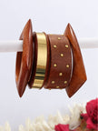 Set of wooden and brass bangles displayed on a white rod with pink flowers in background