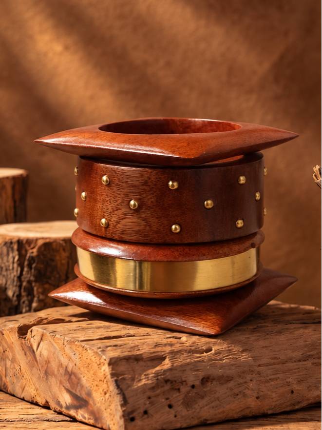 Wooden bangle set with brass studs and gold band stacked flat on a wooden log surface