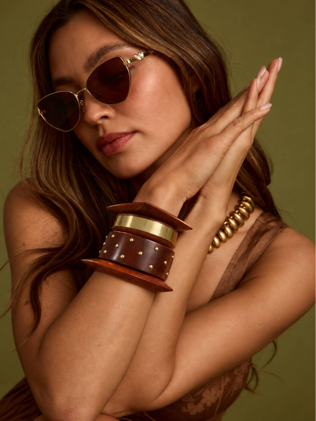 Woman wearing wooden brass stud bangle set on wrist with gold necklace and brown sunglasses