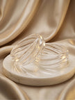 Two clear textured resin bangles with swirled ribbing displayed on a marble disc against champagne satin