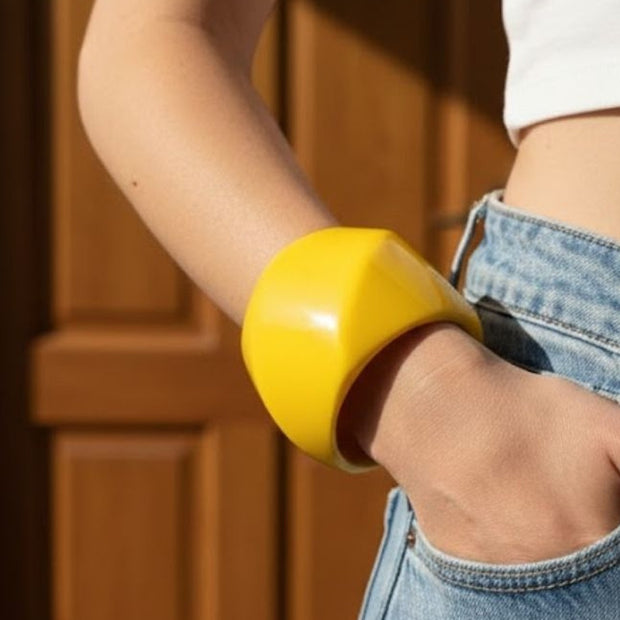 Chunky yellow resin cuff bangle worn on wrist of woman in white crop top and blue denim jeans
