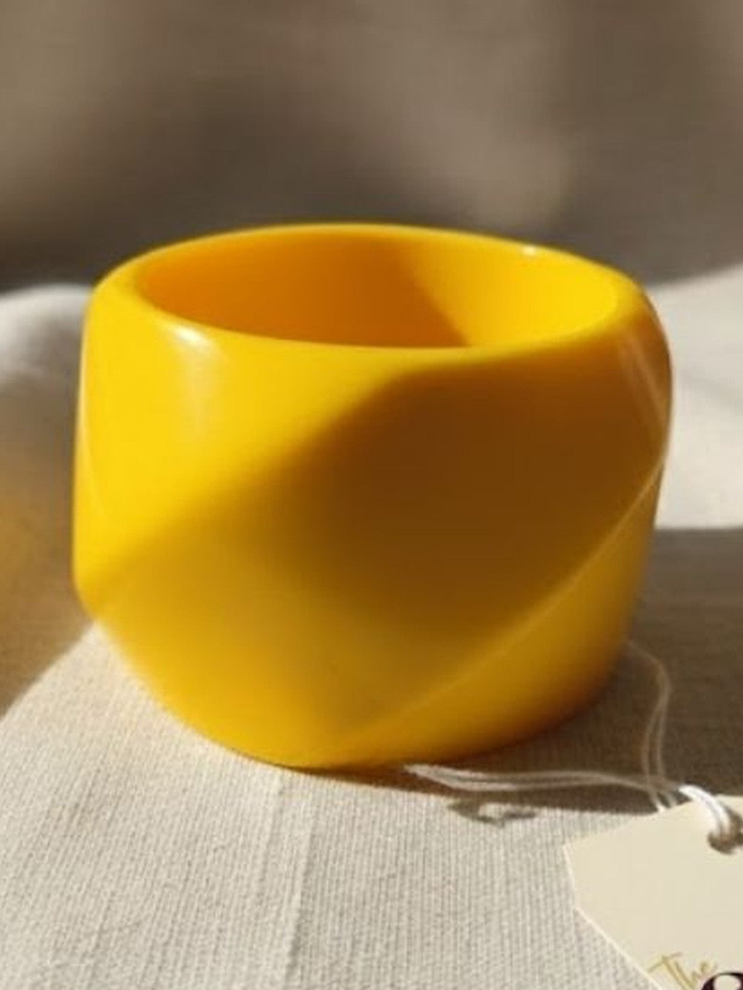Wide yellow resin cuff bangle with high-gloss finish resting on a linen surface with a hang tag