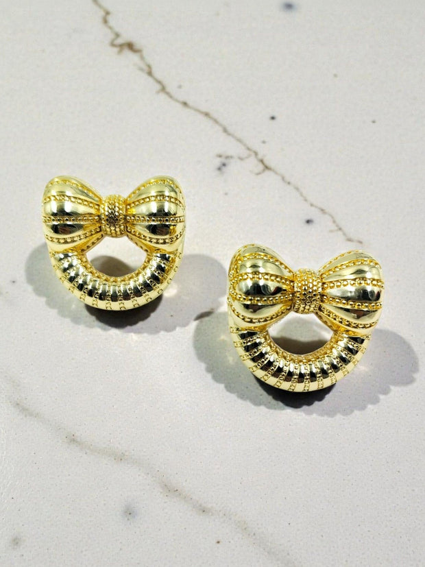 Two gold bow earrings with beaded border and open centre placed on grey marble background