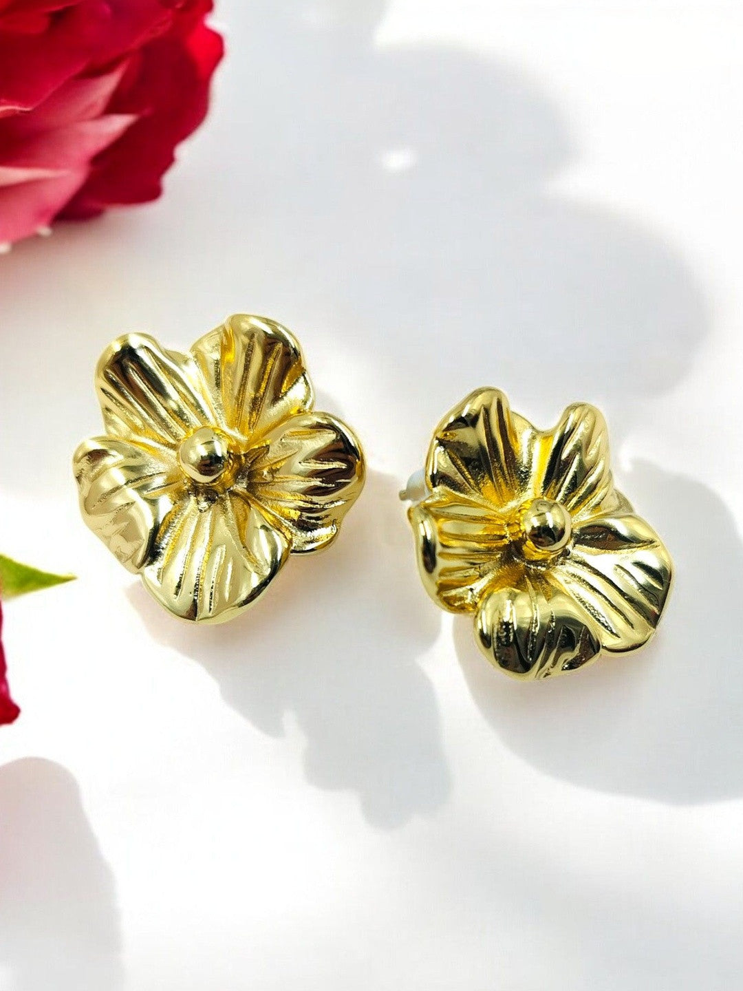 Pair of gold-plated flower stud earrings with ridged petals on white background near a red rose