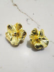 Two gold-plated pansy flower stud earrings placed on a marble surface showing petal detail