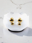 Gold-tone double heart stud earrings resting in white scalloped dish on marble surface in natural light