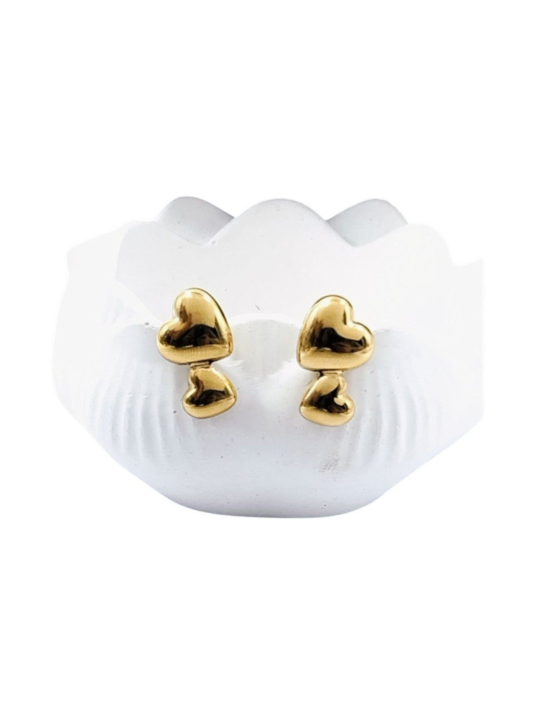 Close-up of polished gold double heart stud earrings on white shell-shaped jewellery holder against white background