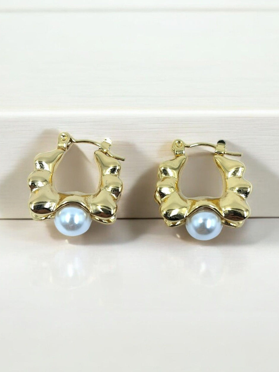 Pair of gold-plated sculpted hoop earrings with white faux pearl drop, displayed on white surface
