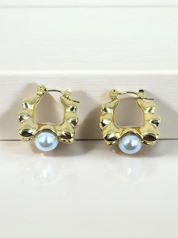 Pair of gold-plated sculpted hoop earrings with white faux pearl drop, displayed on white surface