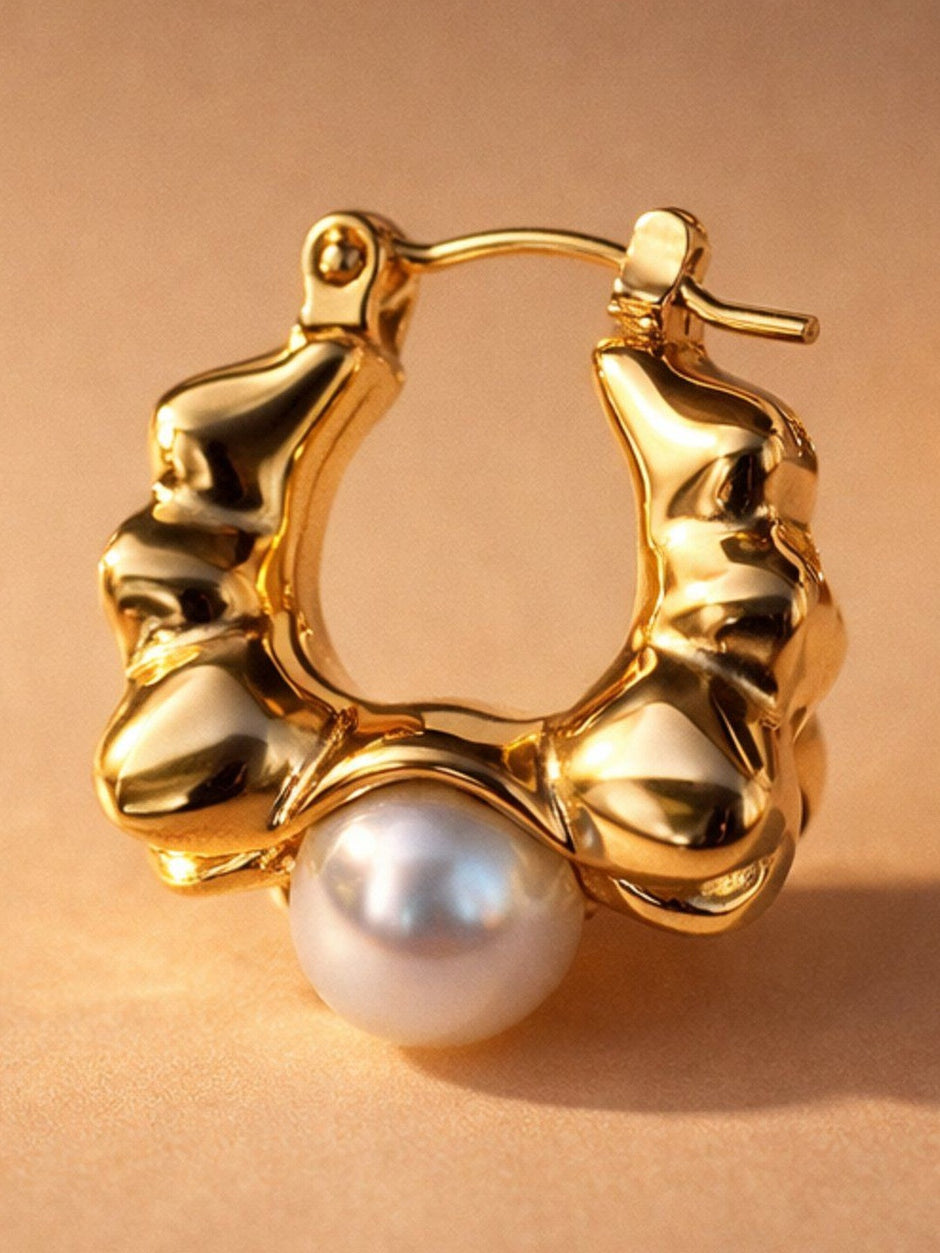 Close-up of single gold-plated rippled hoop earring showing faux pearl and latch-back closure on beige background