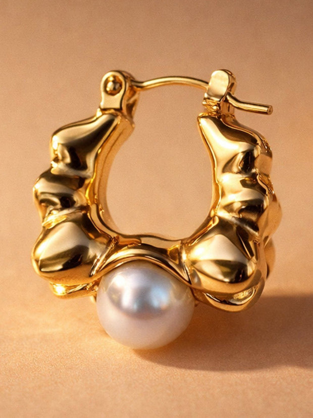 Close-up of single gold-plated rippled hoop earring showing faux pearl and latch-back closure on beige background
