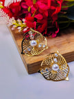 Pair of gold-plated filigree leaf stud earrings with pearl centre and crystal accents on a wooden surface beside red flowers