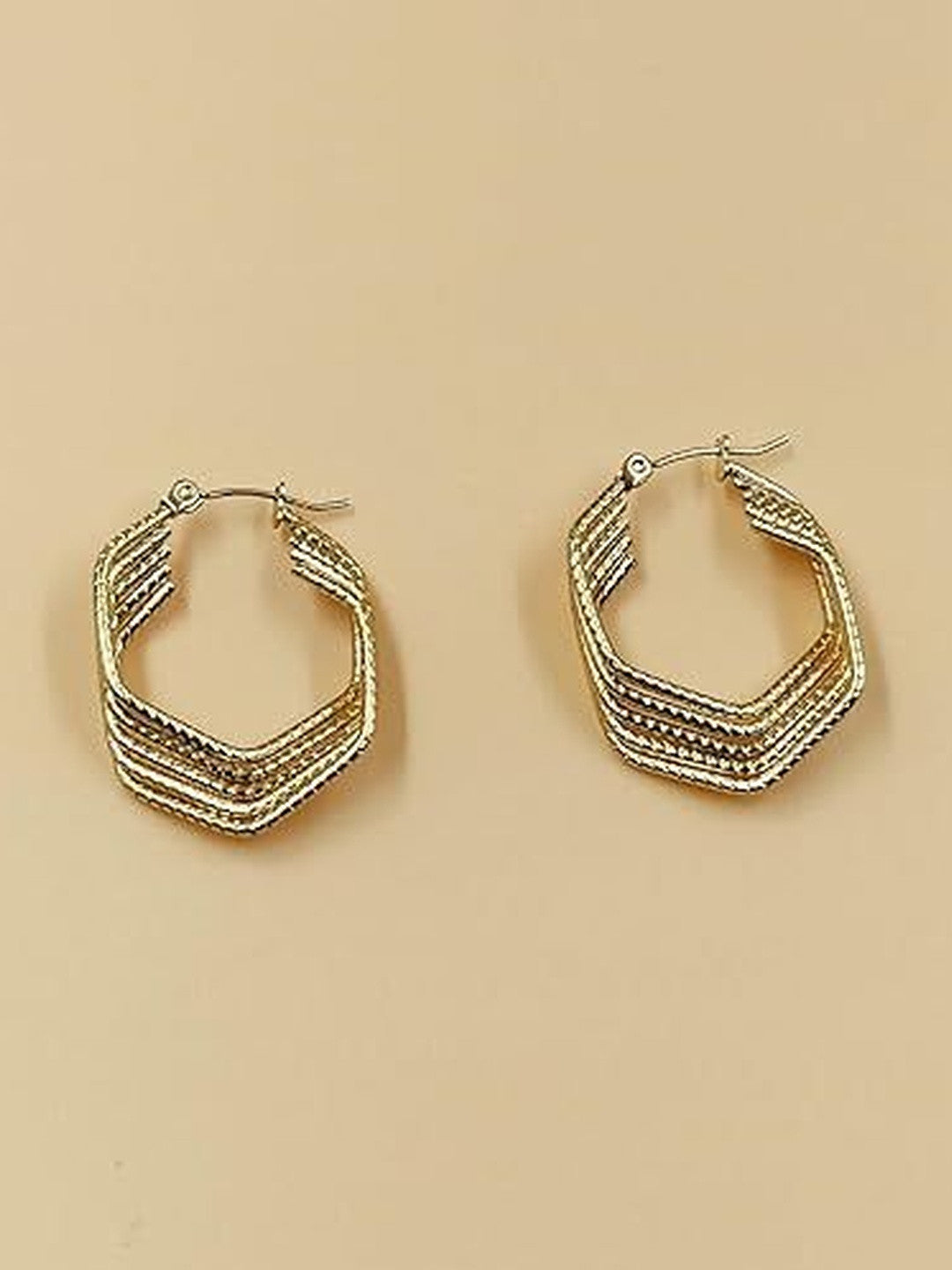 Two gold-tone angular hoop earrings with multi-row ridged design displayed on a beige background