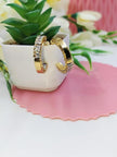 Pair of gold-plated baguette CZ hoop earrings standing upright in a white ceramic planter
