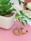 Two gold CZ baguette hoop earrings lying flat on a pink surface beside a succulent plant