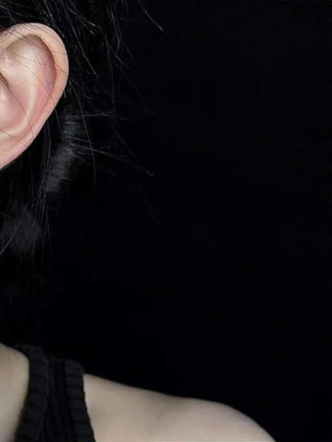 Close-up of ear with dark hair showing no earring worn, styled against black background