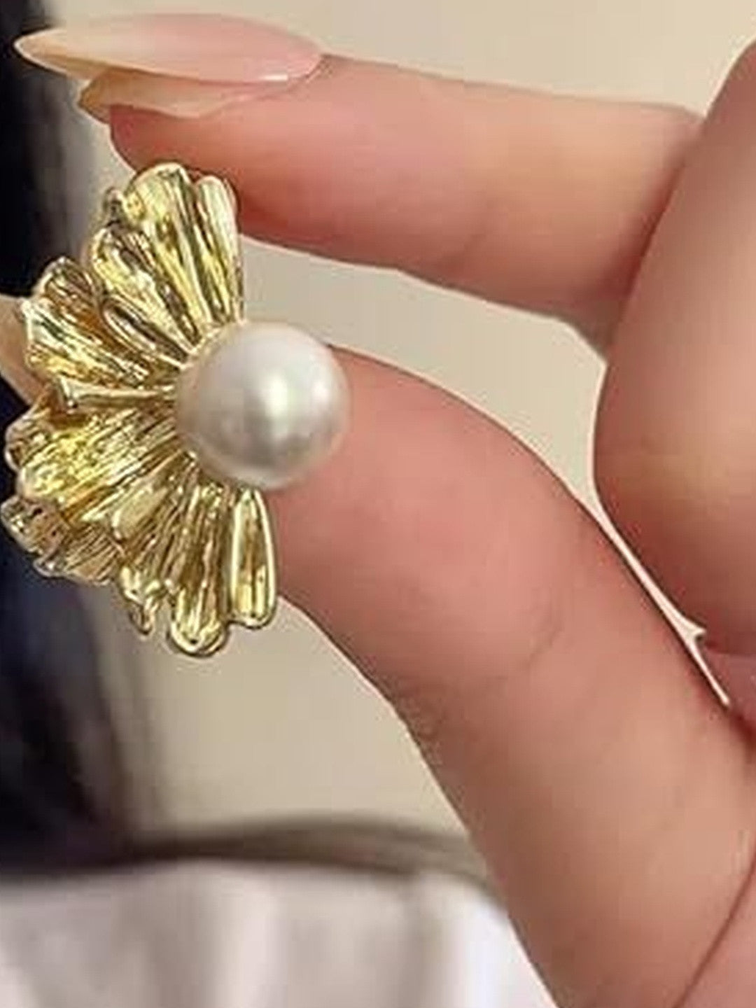 Single gold-plated floral pearl stud earring held between fingers showing ribbed petal texture