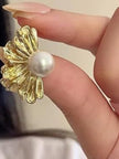 Single gold-plated floral pearl stud earring held between fingers showing ribbed petal texture