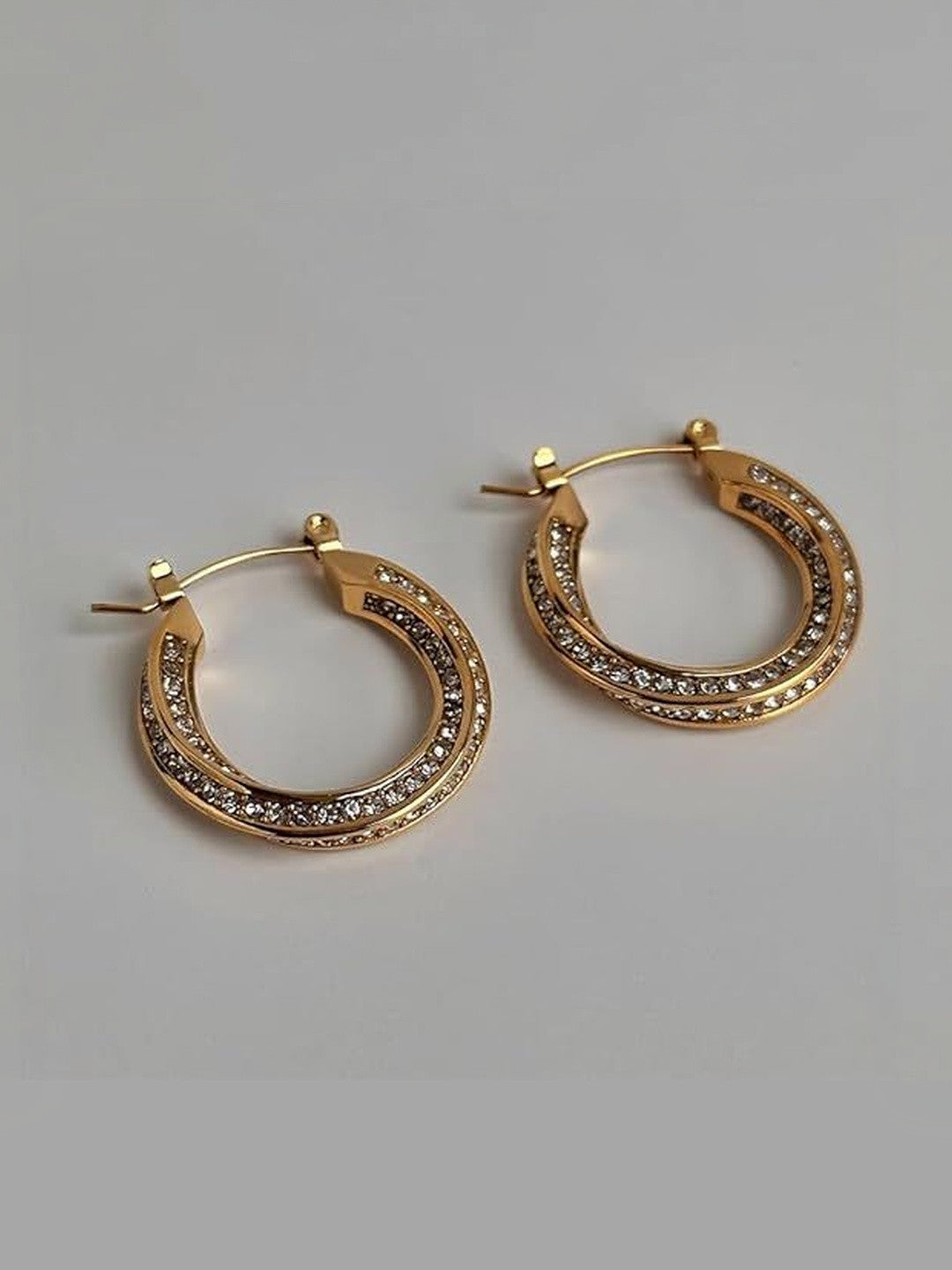 Pair of gold-plated crystal hoop earrings laid flat on a grey surface, showing latch-back closure