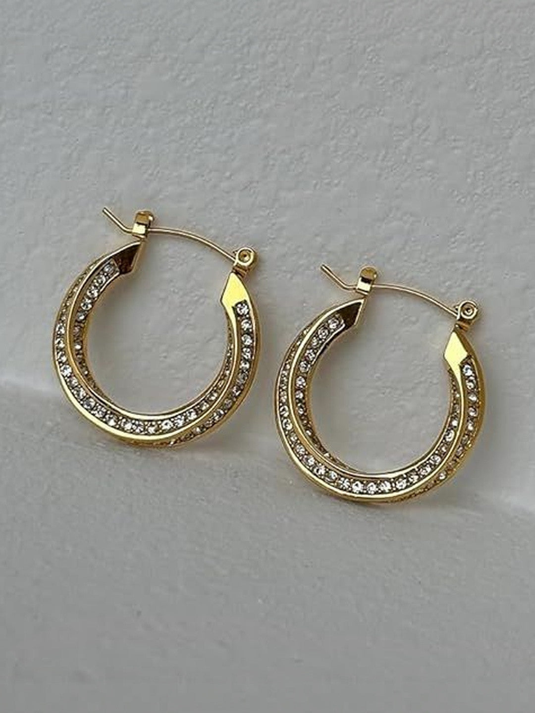 Two gold crystal hoop earrings side by side on a textured white surface, angled view showing double rhinestone rows