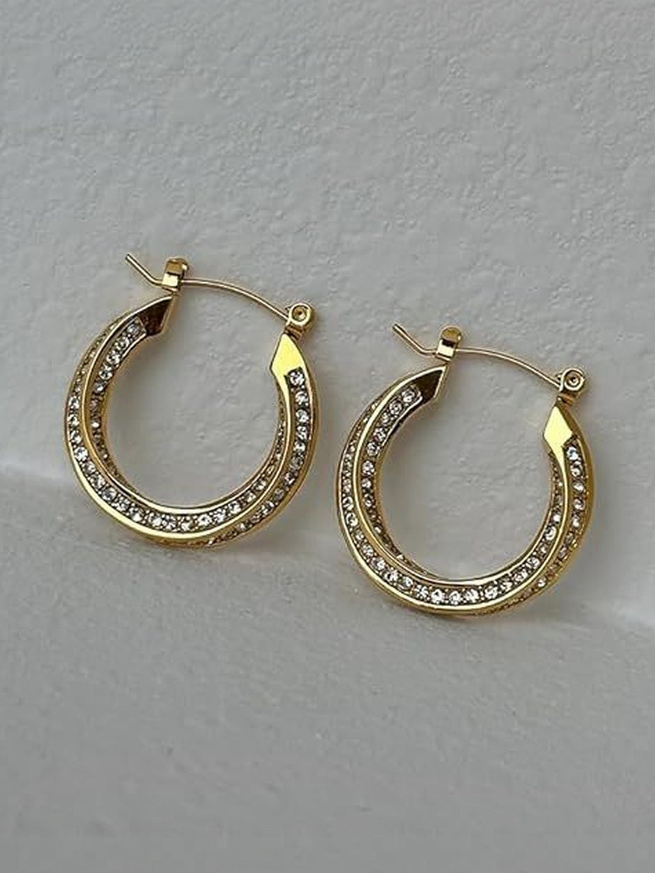 Two gold crystal hoop earrings side by side on a textured white surface, angled view showing double rhinestone rows