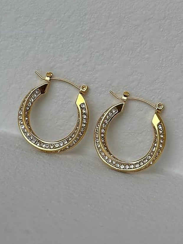 Two gold crystal hoop earrings side by side on a textured white surface, angled view showing double rhinestone rows