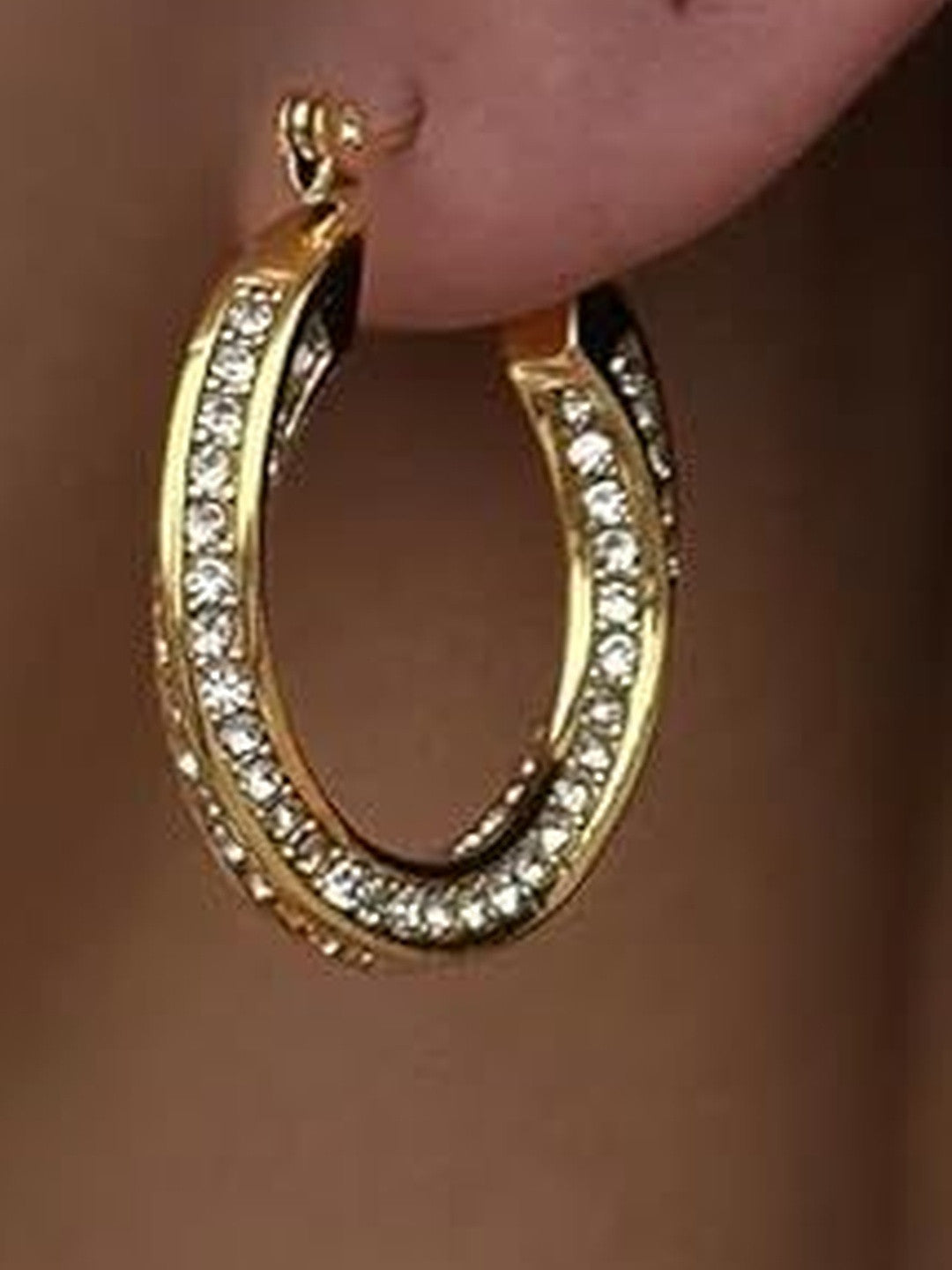 Close-up of a single gold crystal hoop earring worn on a model's earlobe, showing full sparkle and fit