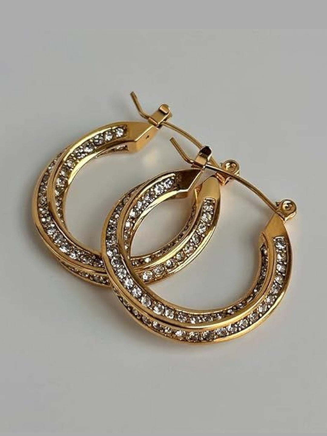 Pair of gold-plated crystal hoops stacked overlapping on grey surface, showing depth and width of the band