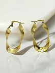 Pair of gold-plated twisted oval hoop earrings resting against a white marble surface