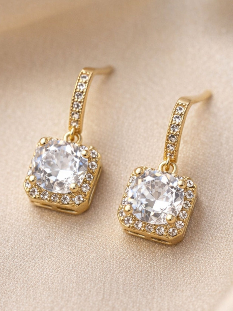 Pair of gold-plated square halo CZ drop earrings laid flat on beige fabric
