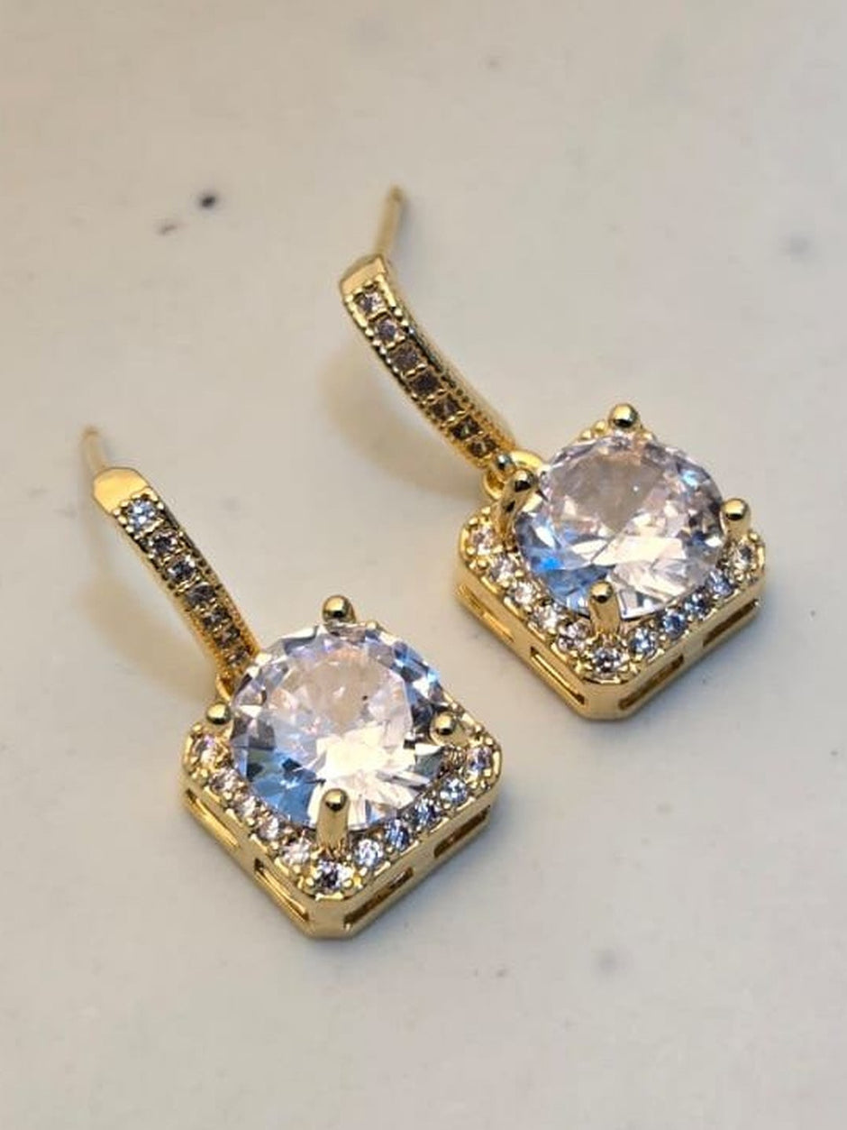 Close-up of two gold-tone CZ halo drop earrings resting on a white marble surface