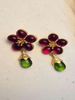 Pair of gold-toned floral earrings with magenta glass petals and green teardrop pendants on a white marble surface
