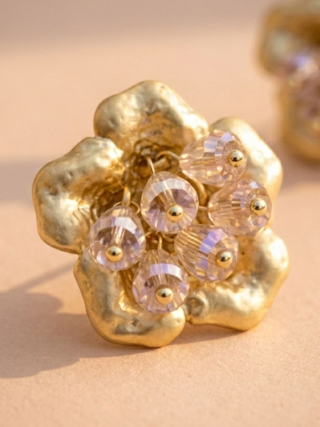 Close-up of one gold-plated flower stud earring with blush crystal bead cluster on peach background