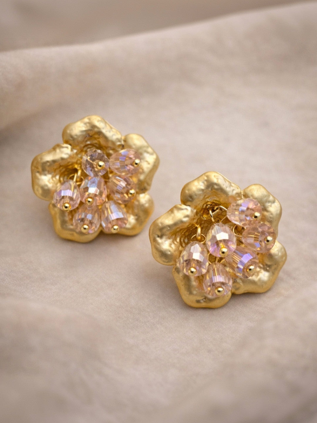 Pair of gold-plated flower stud earrings with crystal bead clusters laid flat on soft grey fabric