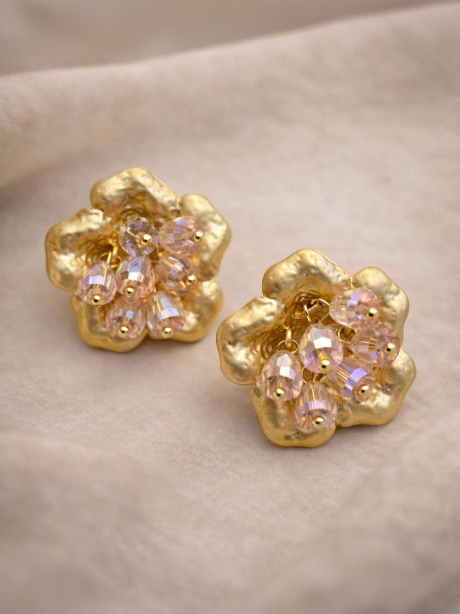 Pair of gold-plated flower stud earrings with crystal bead clusters laid flat on soft grey fabric