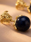 Close-up side view of one gold Medusa stud earring showing deep blue aventurine-effect ball drop