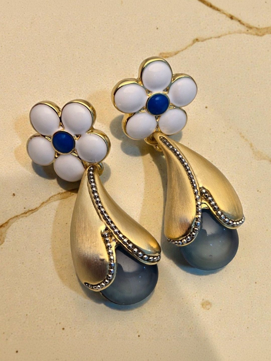 Close-up of both gold-plated floral drop earrings showing brushed gold teardrop and grey pearl globe on marble surface