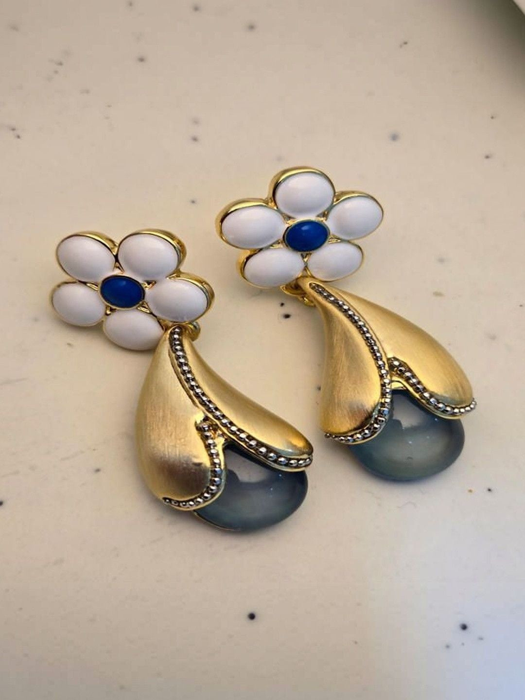 Both gold-plated floral earrings laid flat on white surface showing cobalt blue enamel centre and bead detailing
