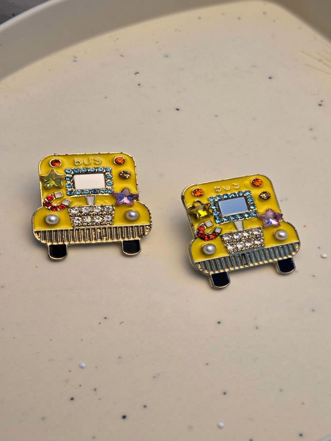 Two yellow enamel bus studs with blue crystal border, red rhinestones, and purple star gems on white background