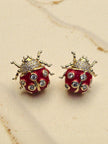 Close-up of two gold-toned red enamel ladybug earrings showing CZ detail and leg texture on a linen surface