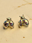 Close-up of gold-plated ladybug stud earrings showing bezel-set red zirconia on a cream marble surface