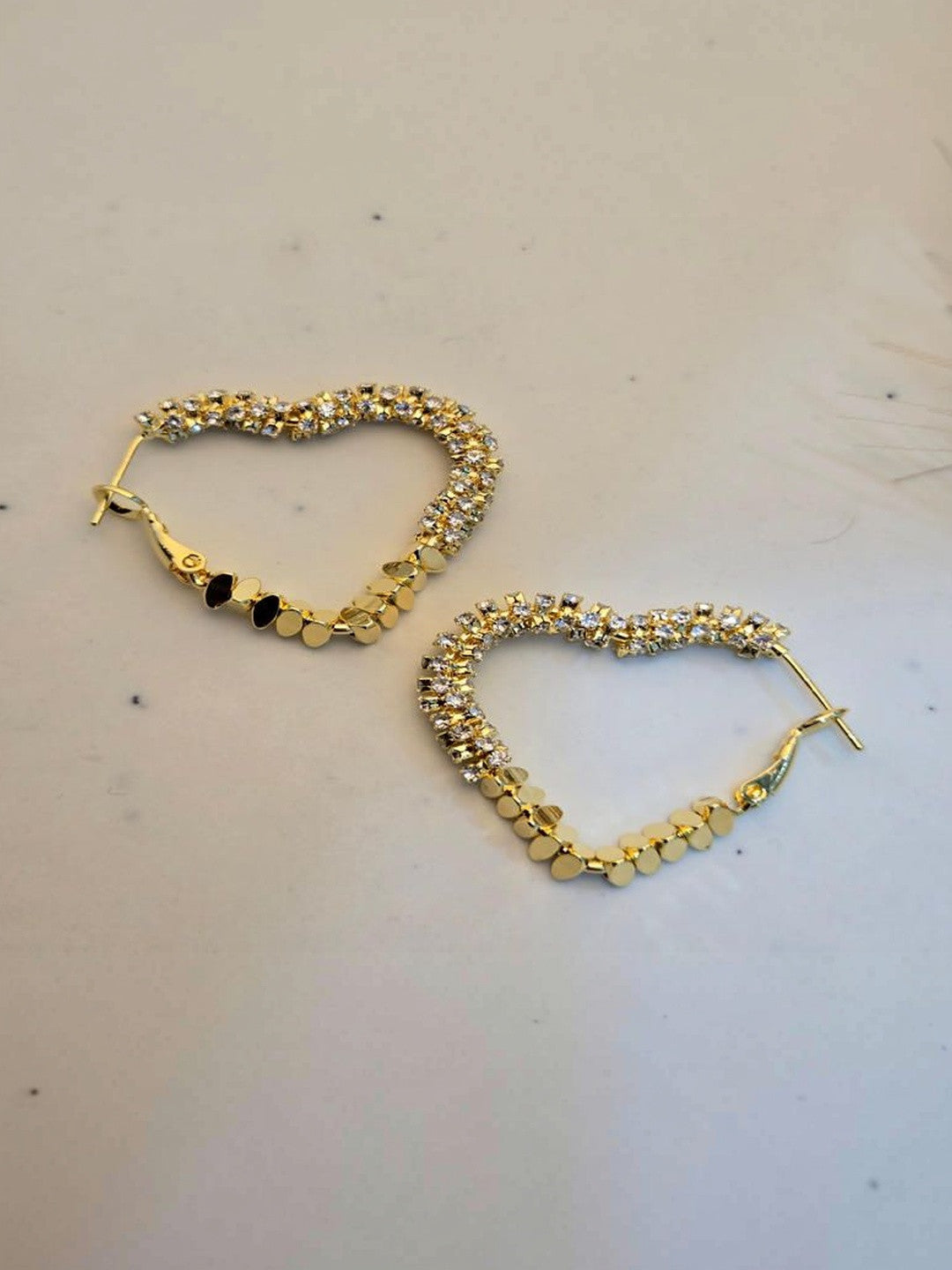 Pair of gold-plated heart hoop earrings with crystal stones laid flat on a white surface